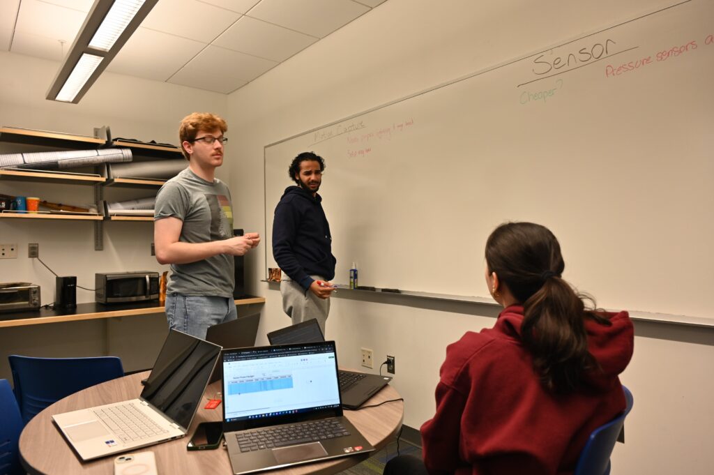 Jeremy and Hisham are standing looking at Jasmine. Hisham looks confused and the team is mid discussion and clarification discussing motion capture set up.