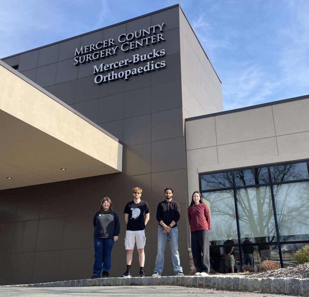 Four college students stand in front of a building with "MercerBucks Orthopedics" on it