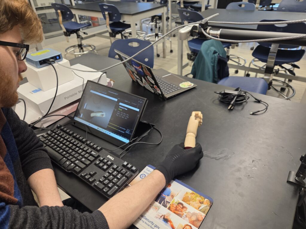 Jeremy Testing the H.O.M.E. application and tendon gliding position identification software with a small wooden model hand in the hook position, one of five in the tendon gliding exercise