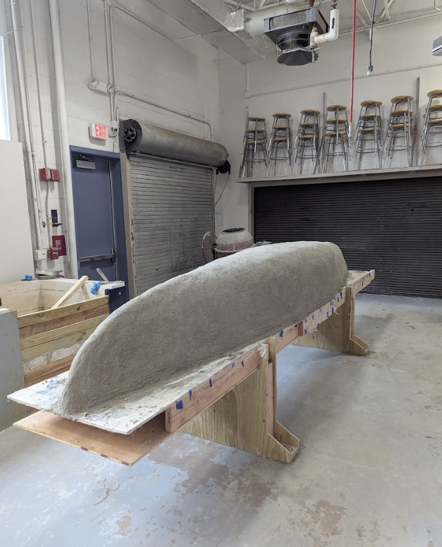 The canoe mold post cast. It remains on the wooden table, but is now covered in light gray concrete.