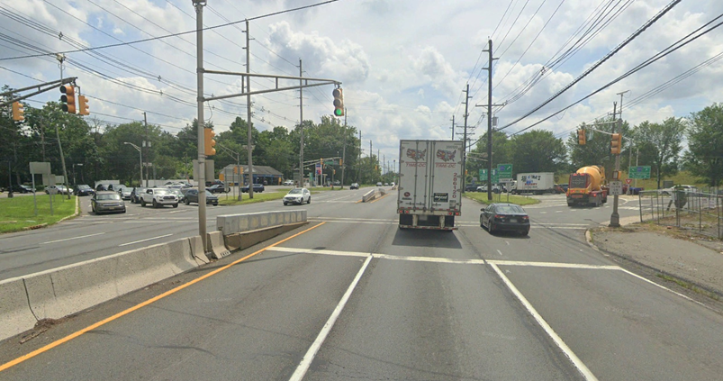 View of the intersection at Washington Road and U.S. Route 1 showing multiple lanes of traffic, a concrete median barrier, overhead traffic signals, and various vehicles.