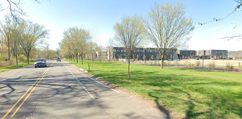 Existing conditions along Washington Road showing a two-lane roadway with vehicles, tree-lined sidewalks, and an adjacent open grassy area. A residential development is visible in the background.