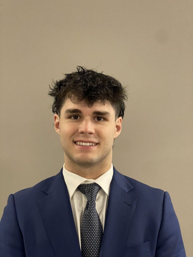 Headshot of Joseph Ricciani smiling at the camera in a blue suit and tie.