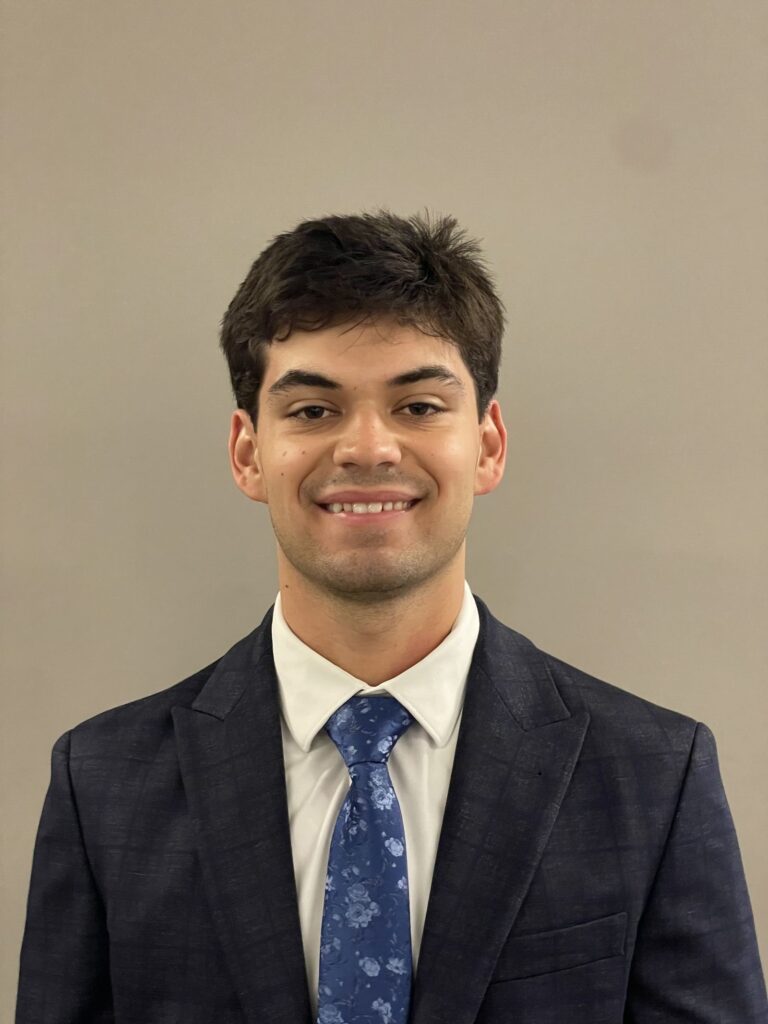 Headshot of Philip Sambucci smiling at the camera wearing a dark blue suit and a light blue tie