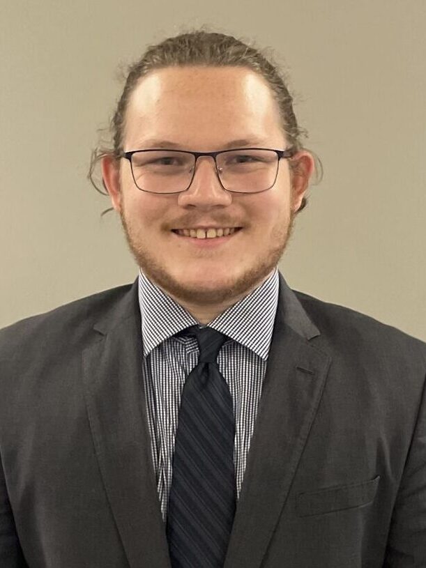 Headshot of Max Dawson smiling at the camera wearing a gray suit with a dark blue tie
